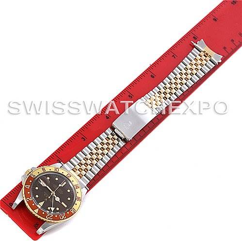 The image shows a Rolex GMT-Master 16753 Men
s Stainless Steel Brown Dial 16753 Men
s Stainless Steel Brown Dial watch laid flat on a red ruler, displaying the watch face and bracelet.