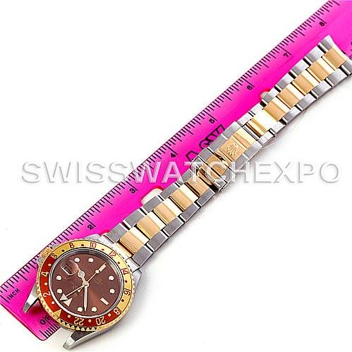 The image shows a top-down view of a Rolex GMT-Master 16713 Men's Stainless Steel Brown Dial 16713 Men's Stainless Steel Brown Dial watch, featuring its bracelet, dial, and bezel next to a pink ruler for scale.