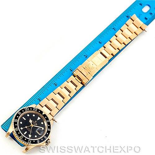 The image shows a top-down view of a Rolex GMT-Master 16758 Men's Stainless Steel Black Dial 16758 Men's Stainless Steel Black Dial watch with a gold bracelet next to a blue ruler for scale.