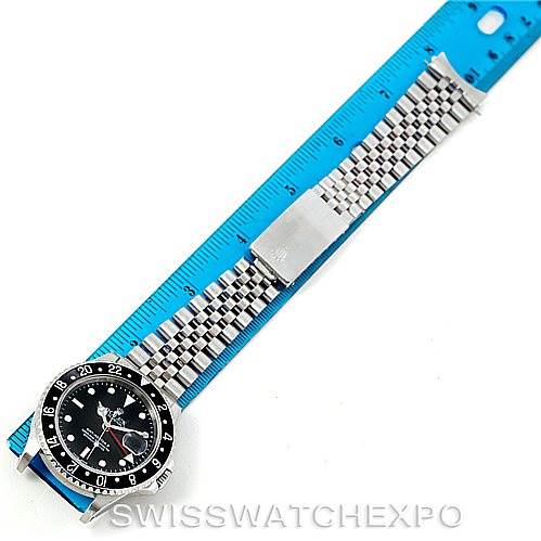 The Rolex GMT-Master 16710 Men's Stainless Steel Black Dial 16710 Men's Stainless Steel Black Dial watch is shown from a top-down angle with its face and metal bracelet laid flat, next to a blue ruler.