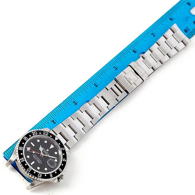 The image shows a Rolex GMT-Master 16710 Men
s Stainless Steel Black Dial 16710 Men
s Stainless Steel Black Dial watch bracelet and case next to a blue ruler for size reference.