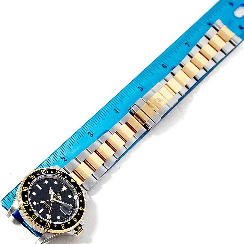 The image shows a Rolex GMT-Master 16713 Men's Stainless Steel Black Dial 16713 Men's Stainless Steel Black Dial watch laid flat beside a blue ruler, highlighting its face, bezel, and two-tone bracelet.