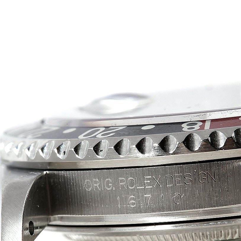 This close-up image of a Rolex GMT-Master 16710 Men's Stainless Steel Black Dial 16710 Men's Stainless Steel Black Dial watch shows part of the bezel, the case, and engraved serial details.
