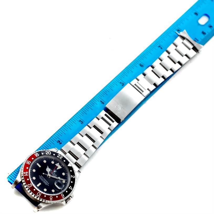 The Rolex GMT-Master 16710 Men's Stainless Steel Black Dial 16710 Men's Stainless Steel Black Dial watch is shown from an overhead angle, displaying its dial, bezel, bracelet, and clasp alongside a ruler.