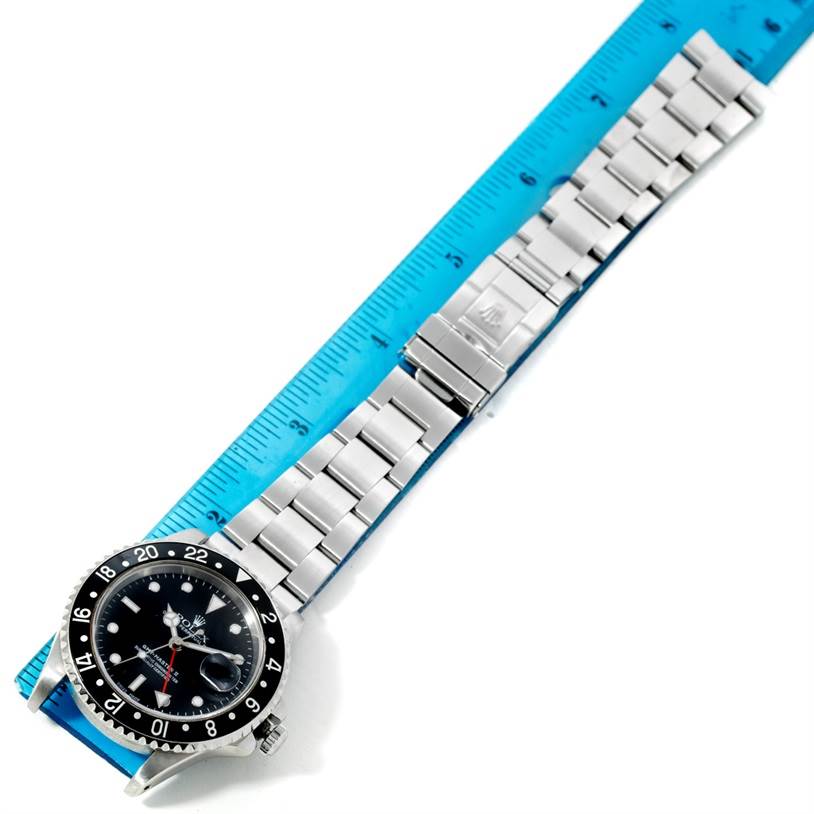 The Rolex GMT-Master 16710 Men's Stainless Steel Black Dial 16710 Men's Stainless Steel Black Dial watch is shown from a top view, displaying the face, bezel, and stainless steel bracelet laid next to a ruler.