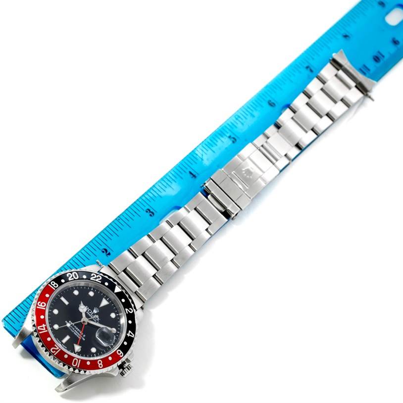 The Rolex GMT-Master 16710 Men's Stainless Steel Black Dial 16710 Men's Stainless Steel Black Dial watch is shown laid flat with its watch face, bezel, and full metal bracelet visible, next to a blue measuring ruler.