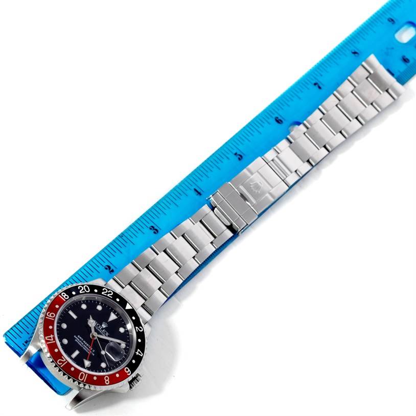 The Rolex GMT-Master 16710 Men's Stainless Steel Black Dial 16710 Men's Stainless Steel Black Dial watch is shown from a top-down angle, next to a blue ruler highlighting its metal bracelet.
