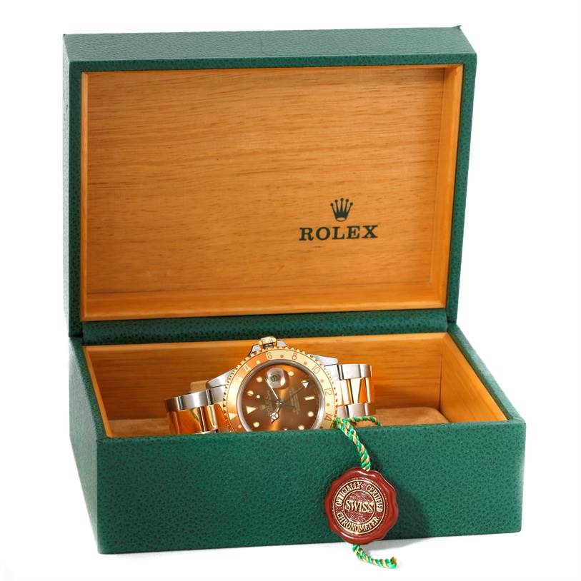The Rolex GMT-Master 16713 Men's Stainless Steel Brown Dial 16713 Men's Stainless Steel Brown Dial watch is shown in an open green and wood display box, with a red "Swiss" tag hanging outside.