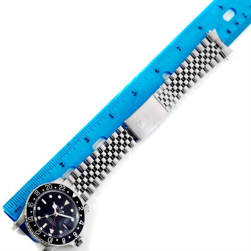 This image shows the Rolex GMT-Master 16750 Men's Stainless Steel Black Dial 16750 Men's Stainless Steel Black Dial watch's face, bezel, bracelet, and clasp, laid next to a ruler for scale.