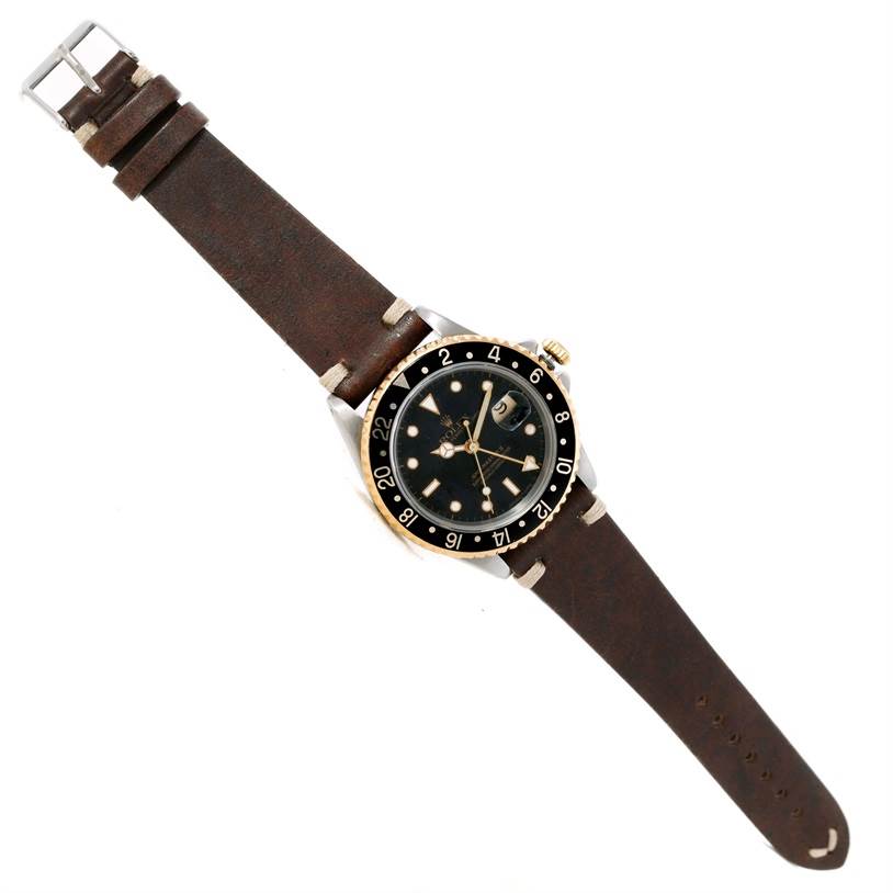 The image shows a top view of a Rolex GMT-Master 16713 Men's Stainless Steel Black Dial 16713 Men's Stainless Steel Black Dial watch with a black dial and a brown leather strap.