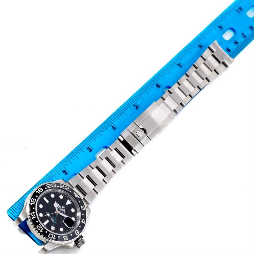 The image shows a top-down view of a Rolex GMT-Master 116710 Men's Stainless Steel Black Dial 116710 Men's Stainless Steel Black Dial watch, including the bracelet and clasp, next to a blue ruler.