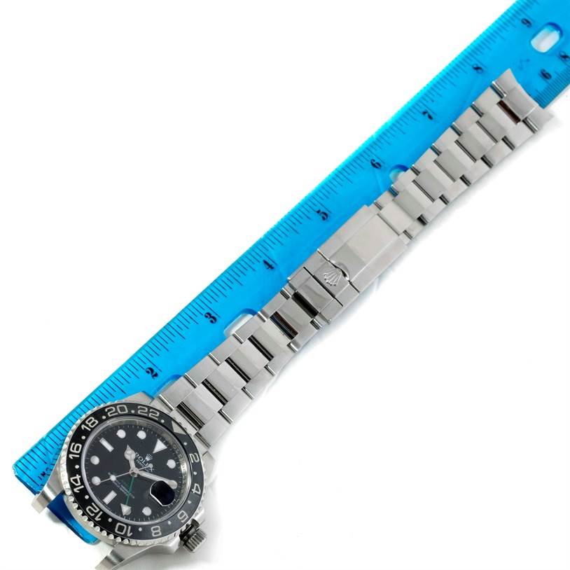 The image shows a top-down view of a Rolex GMT-Master 116710 Men's Stainless Steel Black Dial 116710 Men's Stainless Steel Black Dial watch strapped next to a blue ruler.