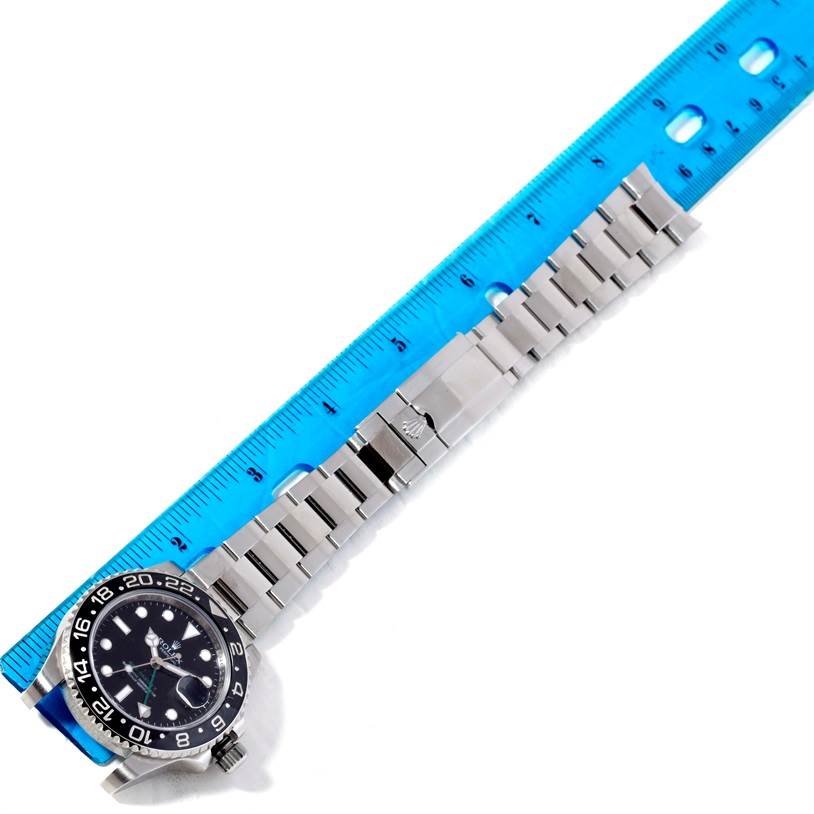 The image shows a horizontal view of the Rolex GMT-Master 116710 Men's Stainless Steel Black Dial 116710 Men's Stainless Steel Black Dial watch with its stainless steel bracelet next to a blue ruler.