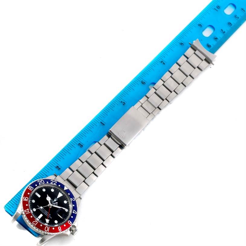 A bird's-eye view of a Rolex GMT-Master 1675 Men's Stainless Steel Black Dial 1675 Men's Stainless Steel Black Dial watch, showing its bracelet, clasp, bezel, and face, with a ruler for scale.