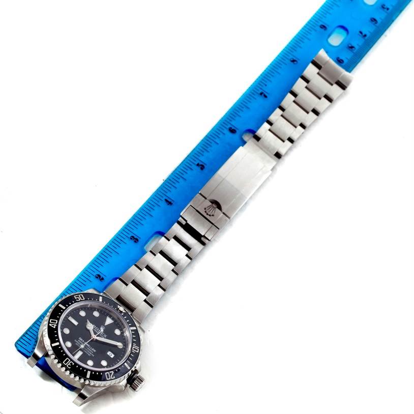 The image shows the Rolex Sea-Dweller 116600 Men
s Stainless Steel Black Dial 116600 Men
s Stainless Steel Black Dial watch laying flat with a blue ruler adjacent to its bracelet for measurement.