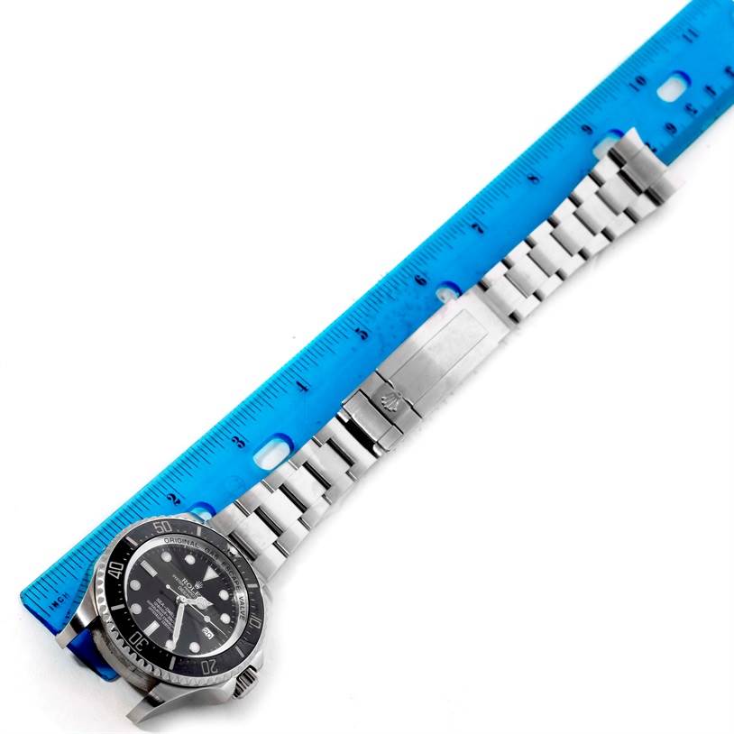 The image shows the Rolex Sea-Dweller 116660 Men's Stainless Steel Black Dial 116660 Men's Stainless Steel Black Dial watch and its stainless steel bracelet laid flat next to a blue ruler from an aerial view.