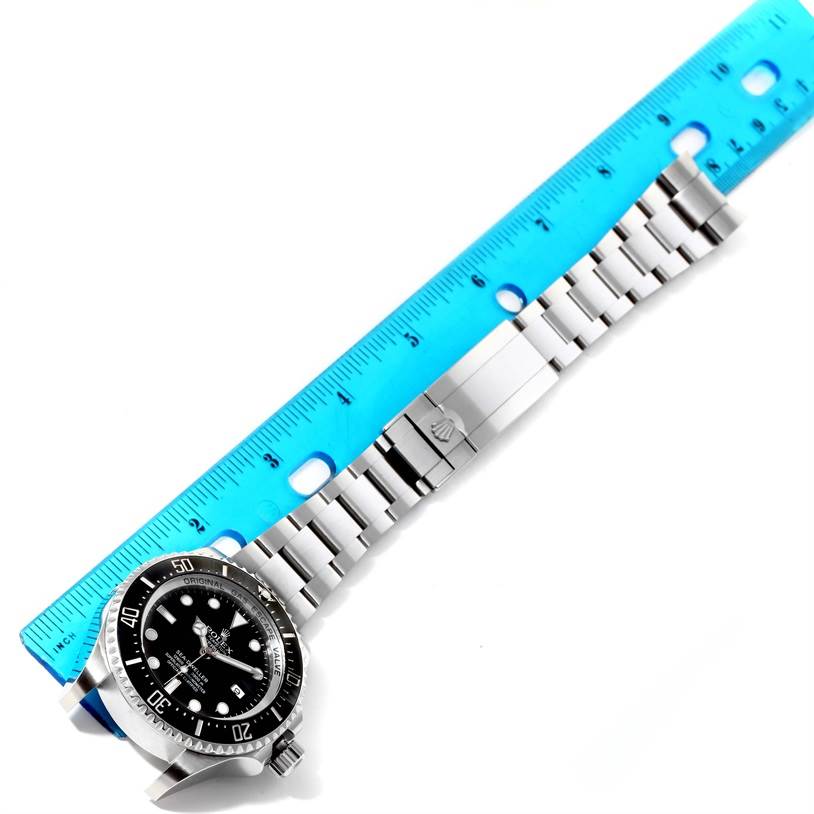 The Rolex Sea-Dweller 116660 Men's Stainless Steel Black Dial 116660 Men's Stainless Steel Black Dial watch is shown from a top-down angle, with focus on the face, bezel, and metal bracelet against a blue ruler.