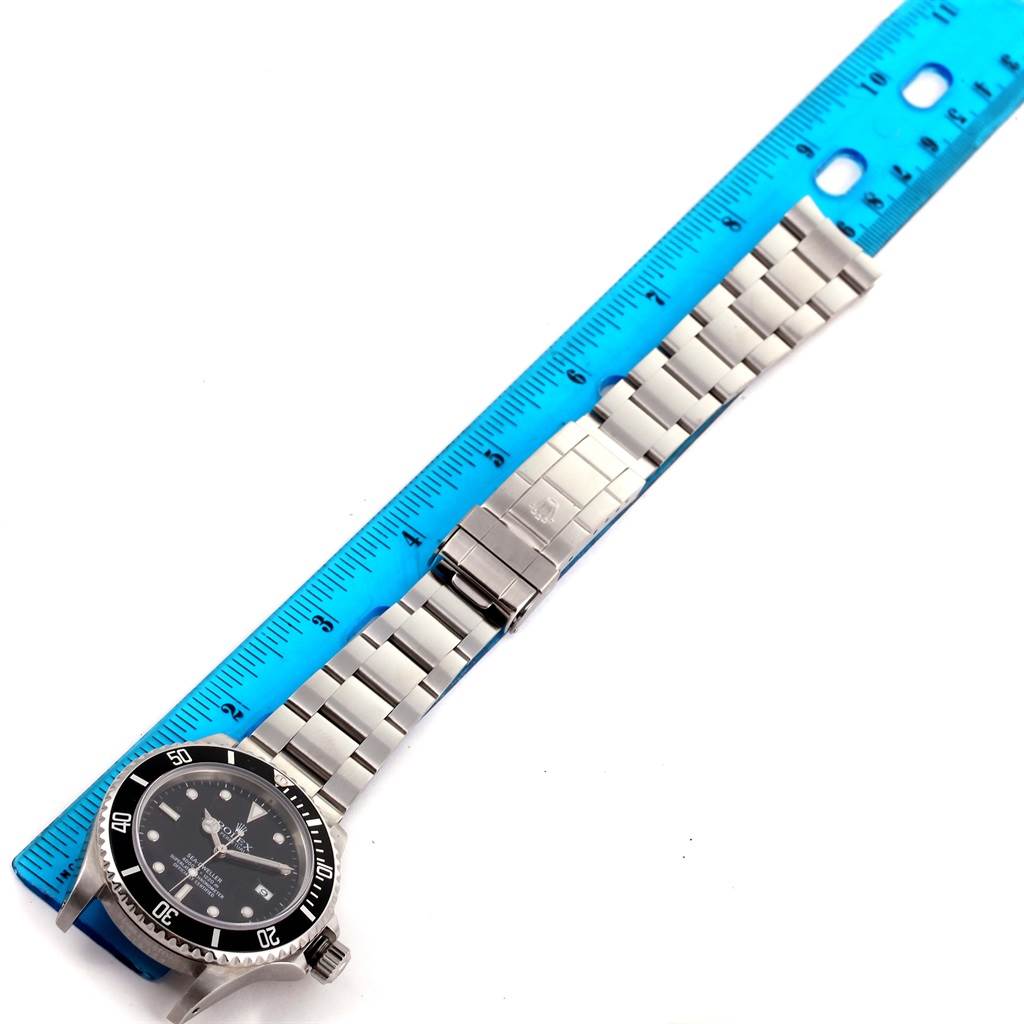 The image shows a top-down view of a Rolex Sea-Dweller 16600 Men
s Stainless Steel Black Dial 16600 Men
s Stainless Steel Black Dial watch with its band extended alongside a blue ruler.