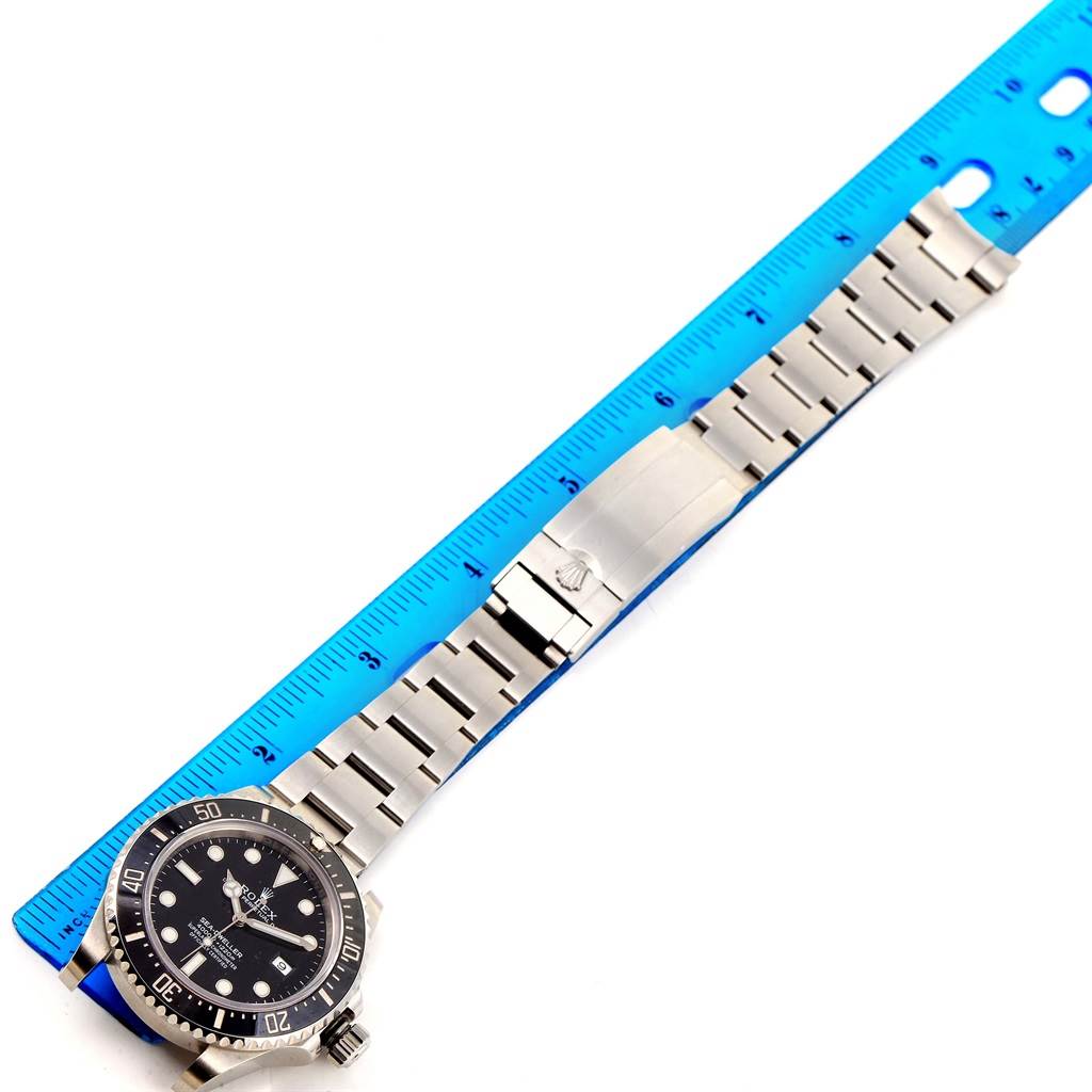 This image shows a top-down view of a Rolex Sea-Dweller 116600 Men's Stainless Steel Black Dial 116600 Men's Stainless Steel Black Dial watch with its bracelet laid out beside a blue ruler for measurement.