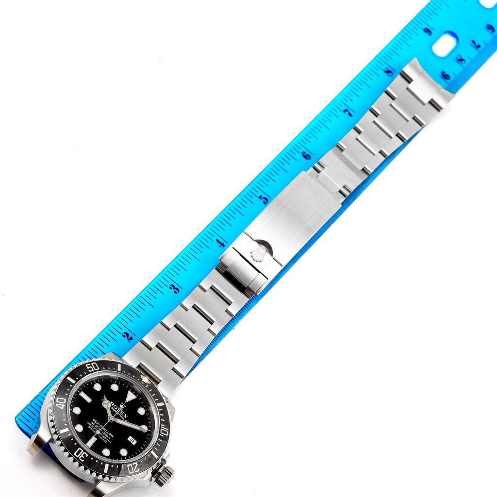 The image shows the Rolex Sea-Dweller 116600 Men
s Stainless Steel Black Dial 116600 Men
s Stainless Steel Black Dial watch face and stainless steel bracelet, laid out alongside a blue ruler for measurement.