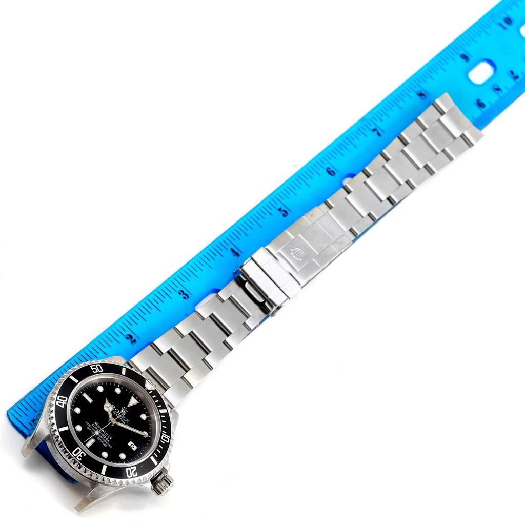 This image shows the Rolex Sea-Dweller 16600 Men
s Stainless Steel Black Dial 16600 Men
s Stainless Steel Black Dial watch face-up with its stainless steel bracelet fully extended next to a blue ruler.