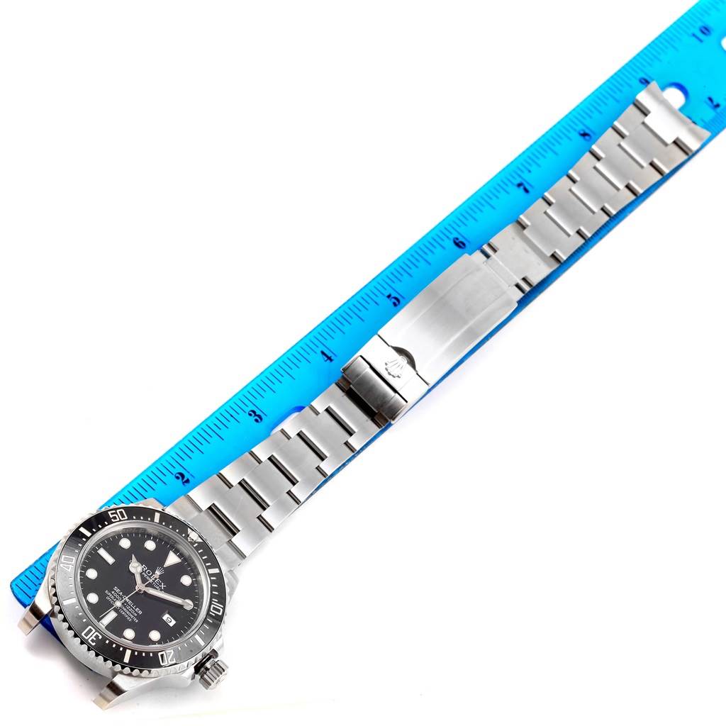 The image shows a top view of a Rolex Sea-Dweller 116600 Men
s Stainless Steel Black Dial 116600 Men
s Stainless Steel Black Dial watch next to a blue ruler, displaying the watch face, bezel, and stainless steel bracelet.