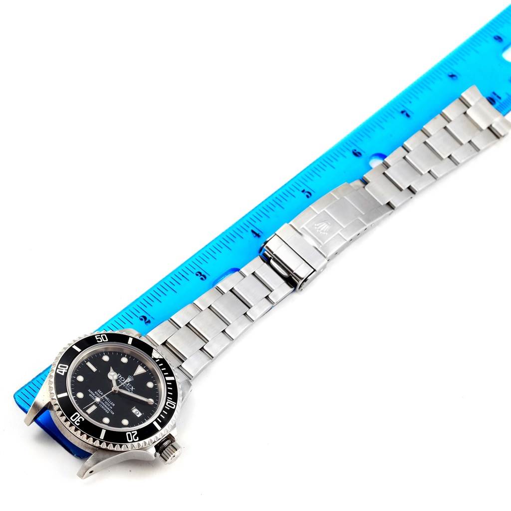 This image shows a Rolex Sea-Dweller 16600 Men
s Stainless Steel Black Dial 16600 Men
s Stainless Steel Black Dial watch laid out flat, with a blue ruler alongside for measurement.