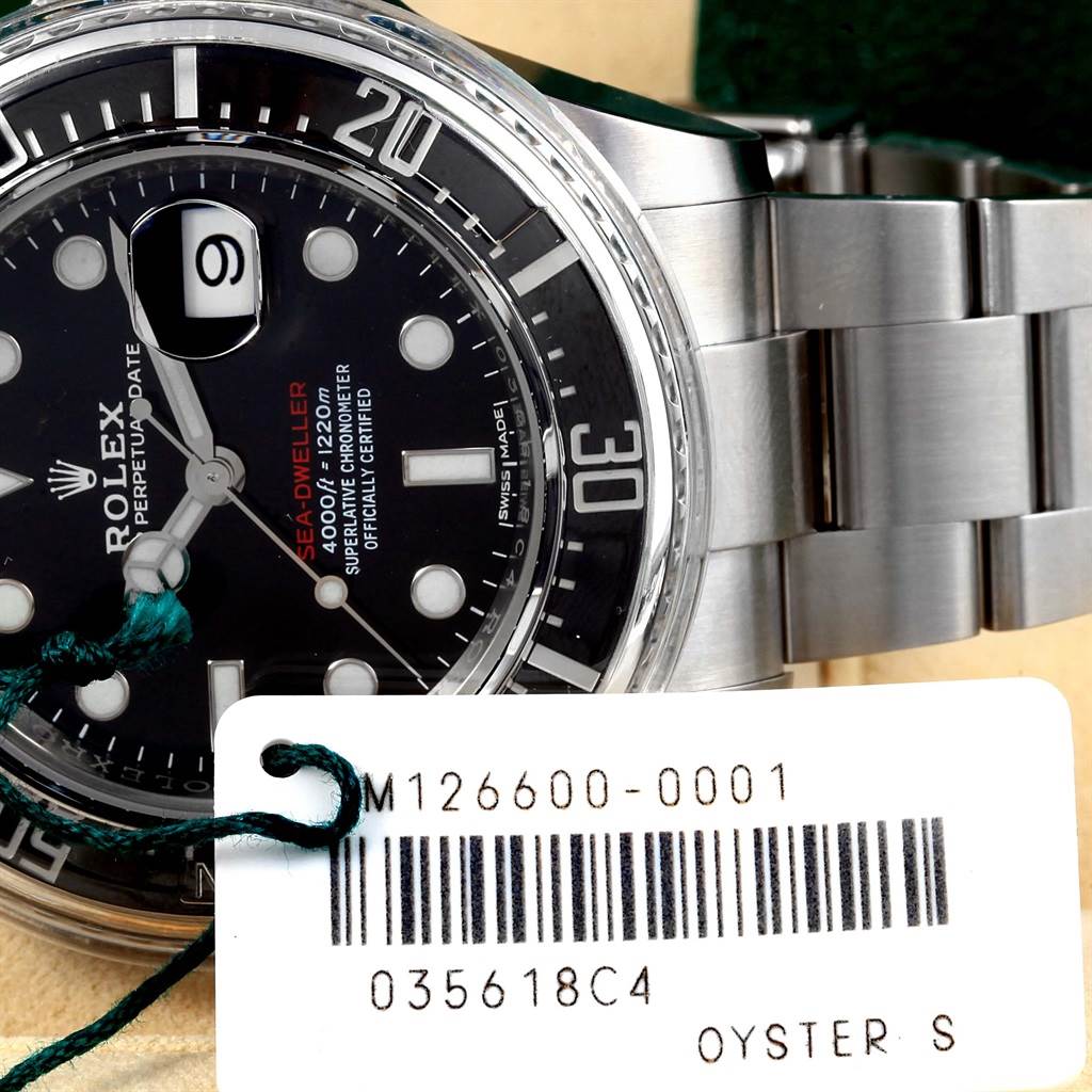 The image shows a close-up of the Rolex Sea-Dweller 126600 Men
s Stainless Steel Black Dial 126600 Men
s Stainless Steel Black Dial dial, bezel, and part of the bracelet alongside a tag with the model number.