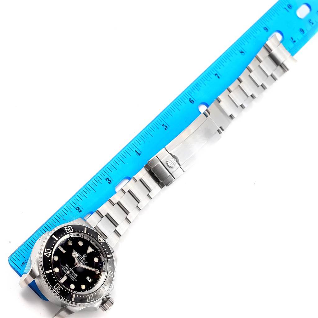 The Rolex Sea-Dweller 116660 Men
s Stainless Steel Black Dial 116660 Men
s Stainless Steel Black Dial watch is shown at a top-down angle, displaying its face, bezel, and band alongside a blue ruler.