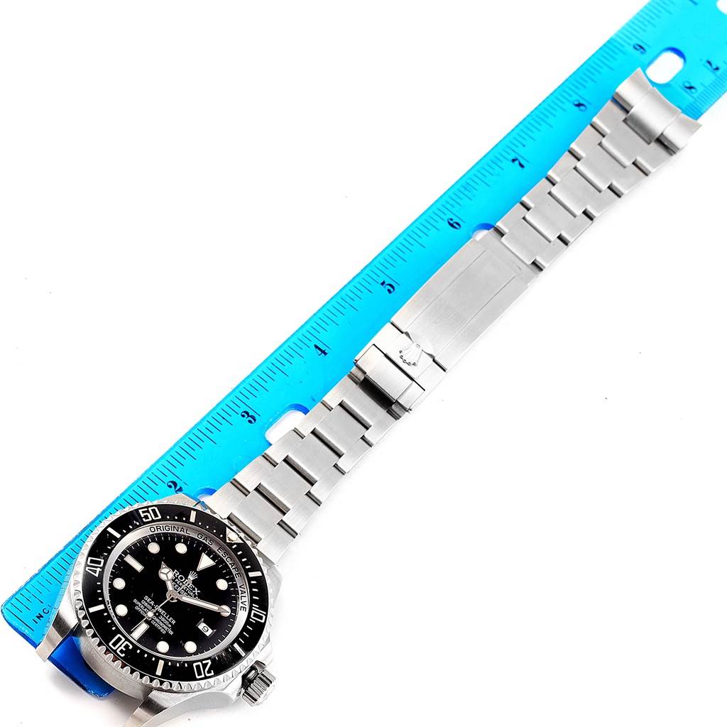 The Rolex Sea-Dweller 116660 Men's Stainless Steel Black Dial 116660 Men's Stainless Steel Black Dial watch is shown lying flat with an extended metal bracelet, partially measured against a blue ruler.