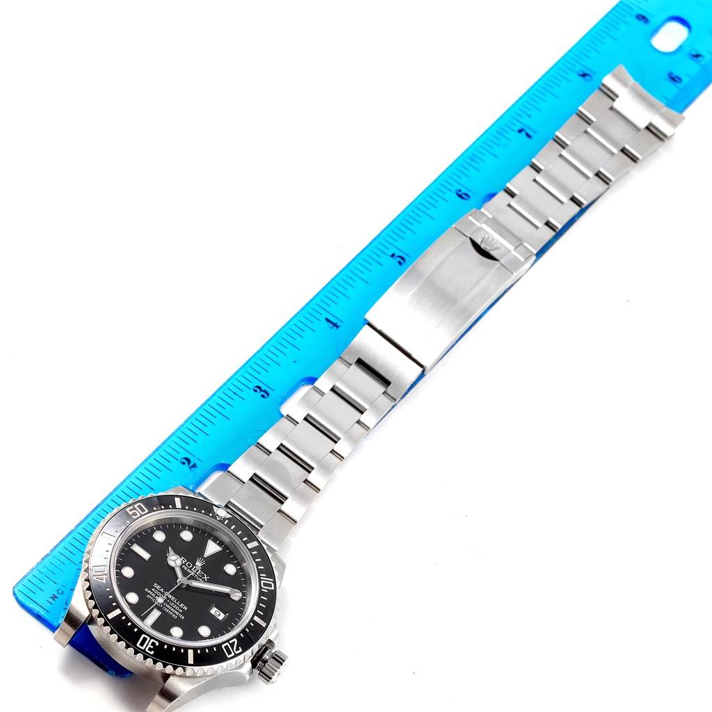 The image shows a top view of a Rolex Sea-Dweller 116600 Men
s Stainless Steel Black Dial 116600 Men
s Stainless Steel Black Dial watch, including its face, bezel, and metal bracelet next to a blue ruler.