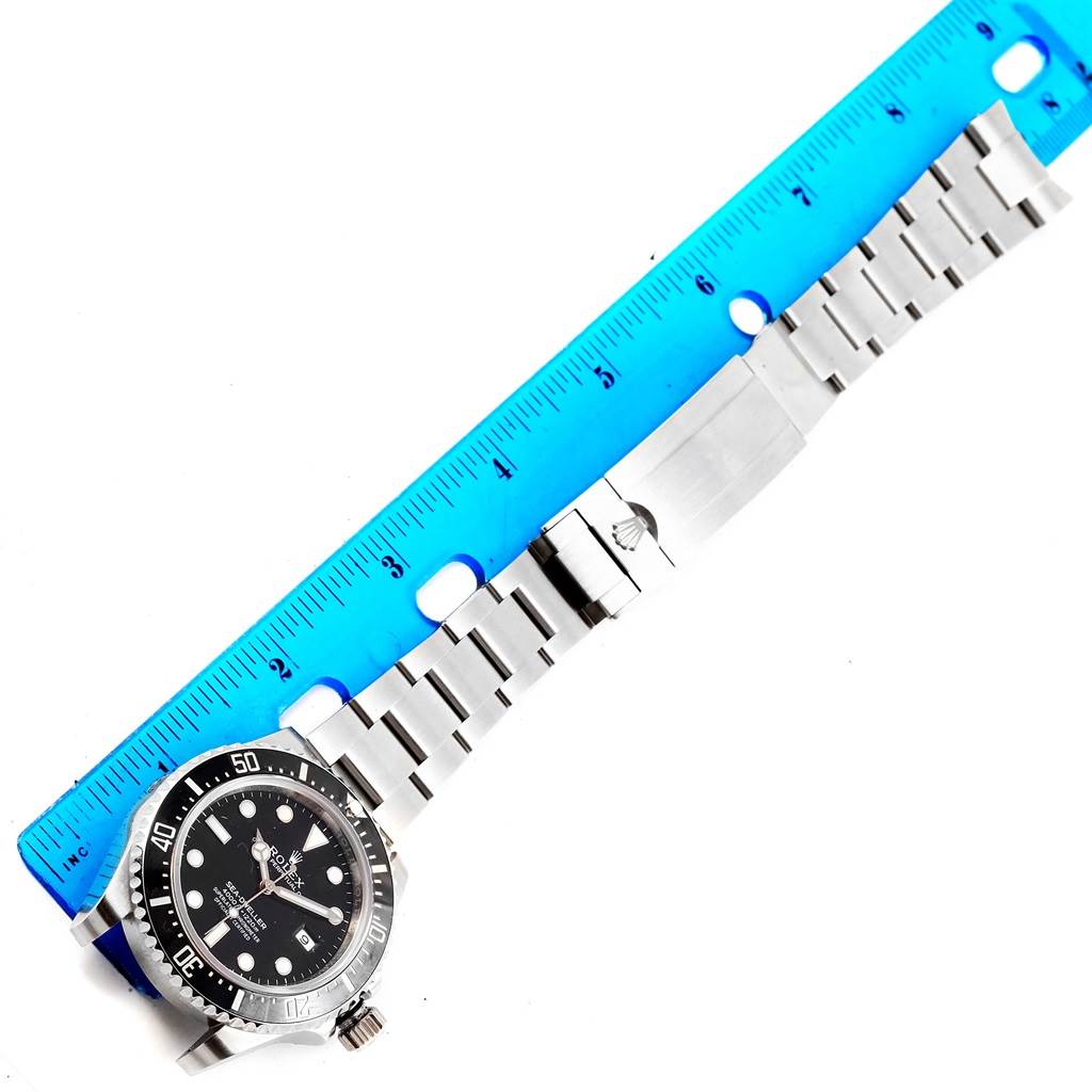 The Rolex Sea-Dweller 116600 Men's Stainless Steel Black Dial 116600 Men's Stainless Steel Black Dial watch is shown from an overhead angle, displaying its face, bezel, and metal bracelet against a blue ruler.