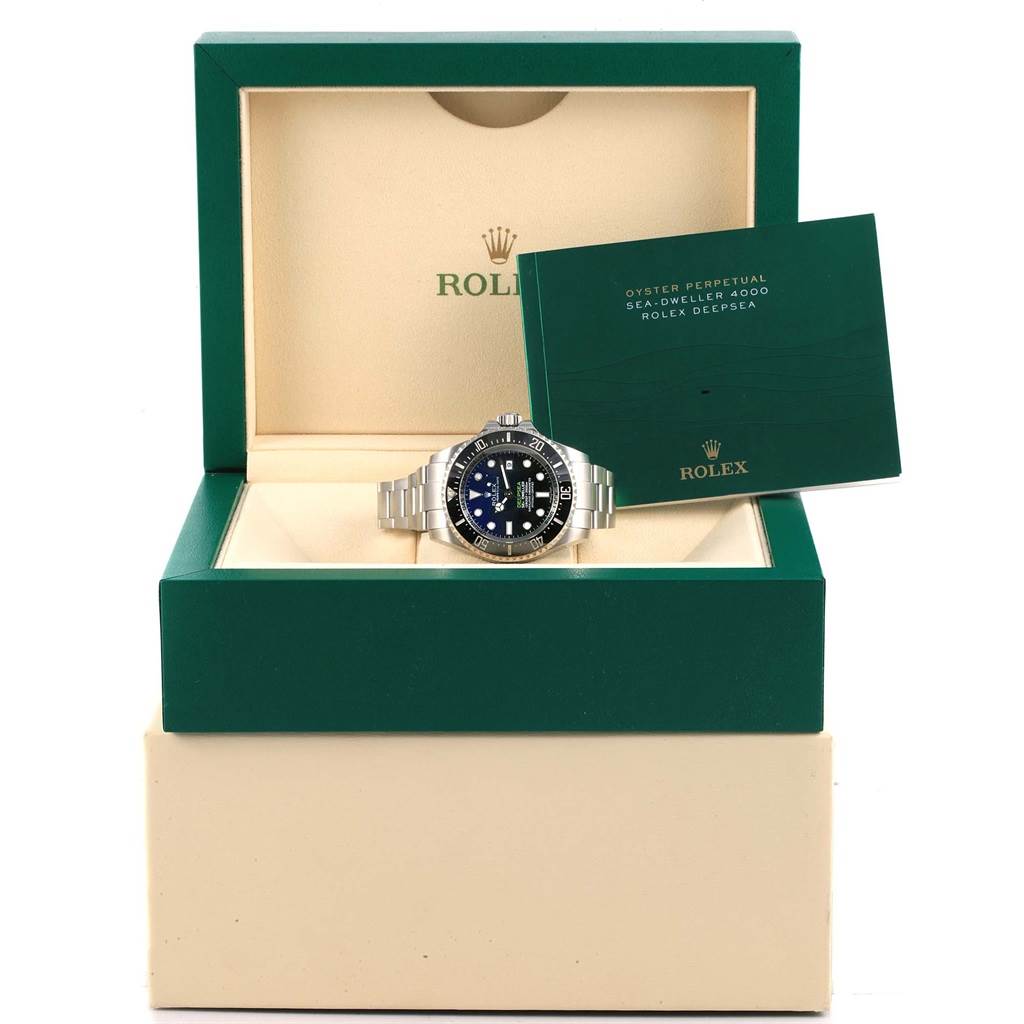 The Rolex Sea-Dweller 116660 Men's Stainless Steel Blue Dial 116660 Men's Stainless Steel Blue Dial watch is displayed front-facing in an open green and beige box with accompanying booklet.