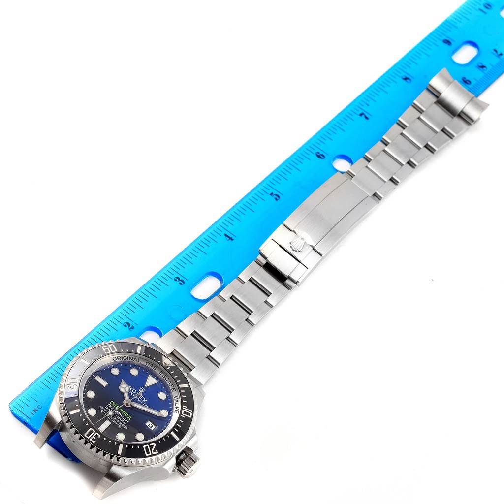 The image shows a Rolex Sea-Dweller 116660 Men's Stainless Steel Blue Dial 116660 Men's Stainless Steel Blue Dial watch laid flat next to a blue ruler, highlighting its face, bezel, and metal bracelet.