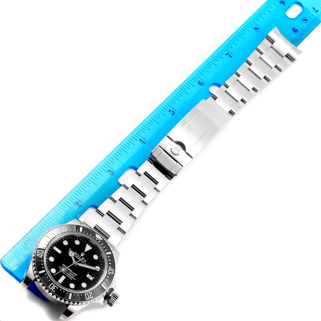 The image shows a top view of the Rolex Sea-Dweller 116600 Men
s Stainless Steel Black Dial 116600 Men
s Stainless Steel Black Dial watch, including its dial, bezel, and bracelet, next to a blue ruler.