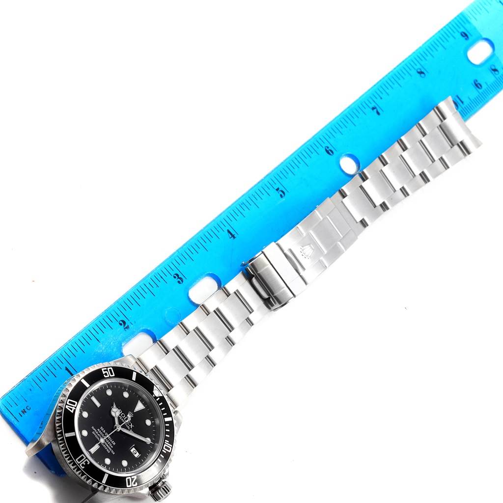 This image shows a Rolex Sea-Dweller 16600 Men
s Stainless Steel Black Dial 16600 Men
s Stainless Steel Black Dial watch laid flat with its bracelet extended alongside a blue ruler.