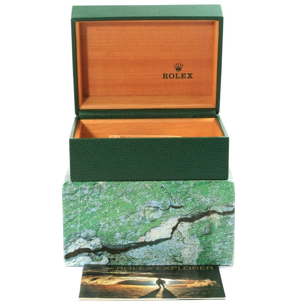 The image shows an open Rolex Sea-Dweller 16600 Men
s Stainless Steel Black Dial 16600 Men
s Stainless Steel Black Dial watch box with a green exterior and wood interior, placed on a themed box.