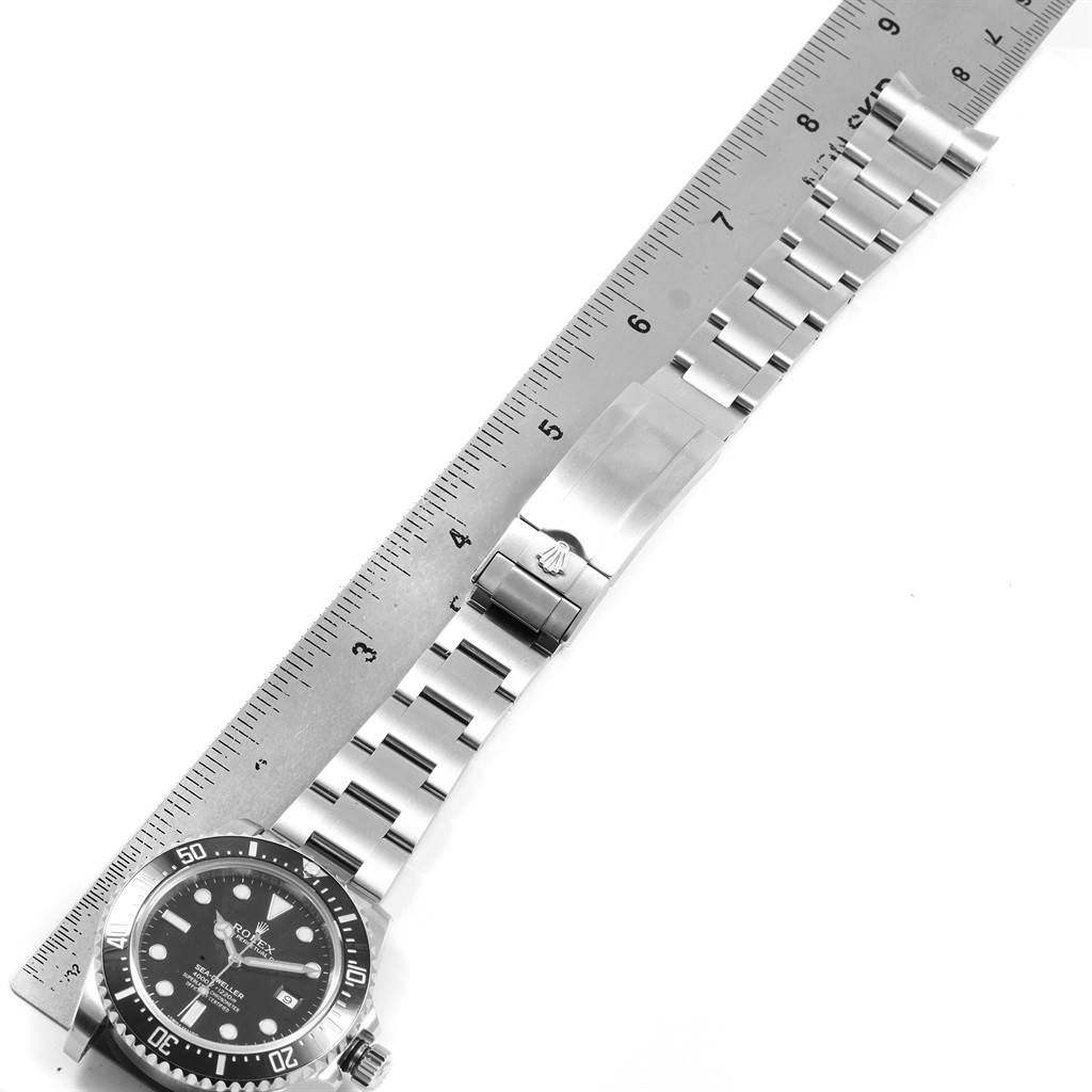The image shows a top-down view of a Rolex Sea-Dweller 116600 Men
s Stainless Steel Black Dial 116600 Men
s Stainless Steel Black Dial watch, focusing on the face, bezel, and stainless steel bracelet alongside a ruler.
