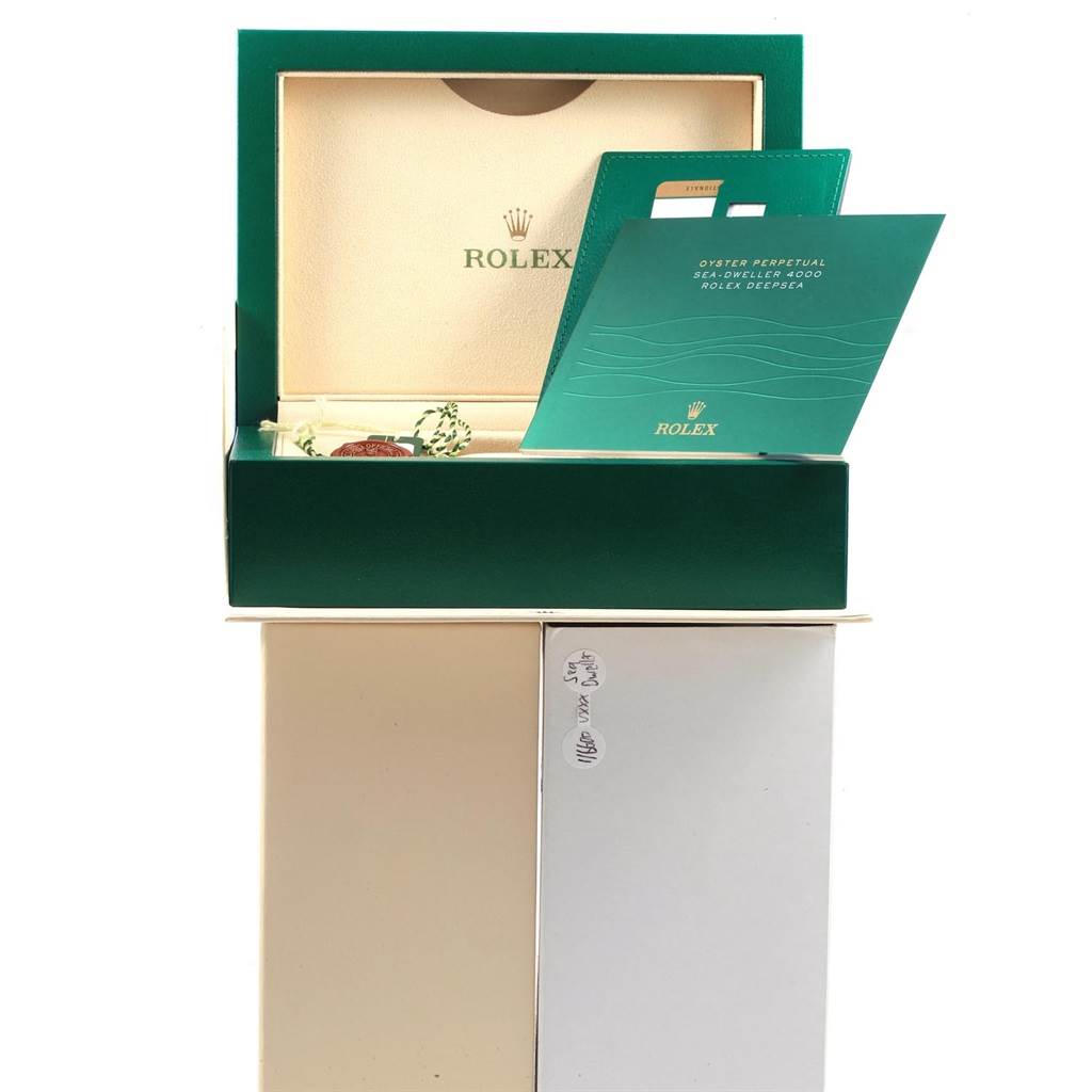 The image shows the open packaging of a Rolex Sea-Dweller 116600 Men
s Stainless Steel Black Dial 116600 Men
s Stainless Steel Black Dial watch, including the box, warranty card, and booklet.