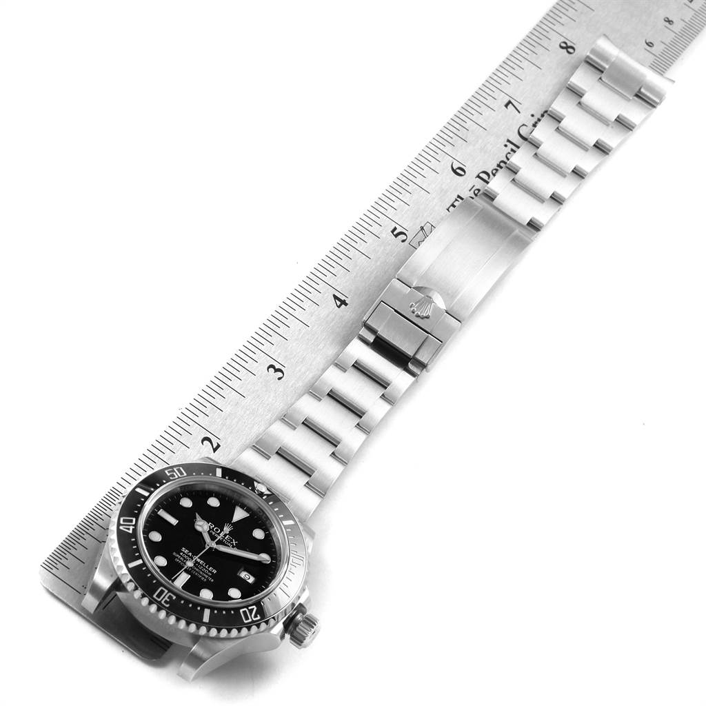 The image shows a top-down view of a Rolex Sea-Dweller 116600 Men
s Stainless Steel Black Dial 116600 Men
s Stainless Steel Black Dial watch with a stainless steel bracelet next to a ruler for measurement.