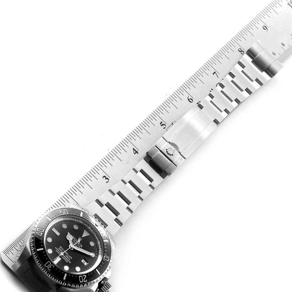 The image shows a top-down view of a Rolex Sea-Dweller 116660 Men
s Stainless Steel Black Dial 116660 Men
s Stainless Steel Black Dial watch with its stainless steel bracelet laid against a ruler.