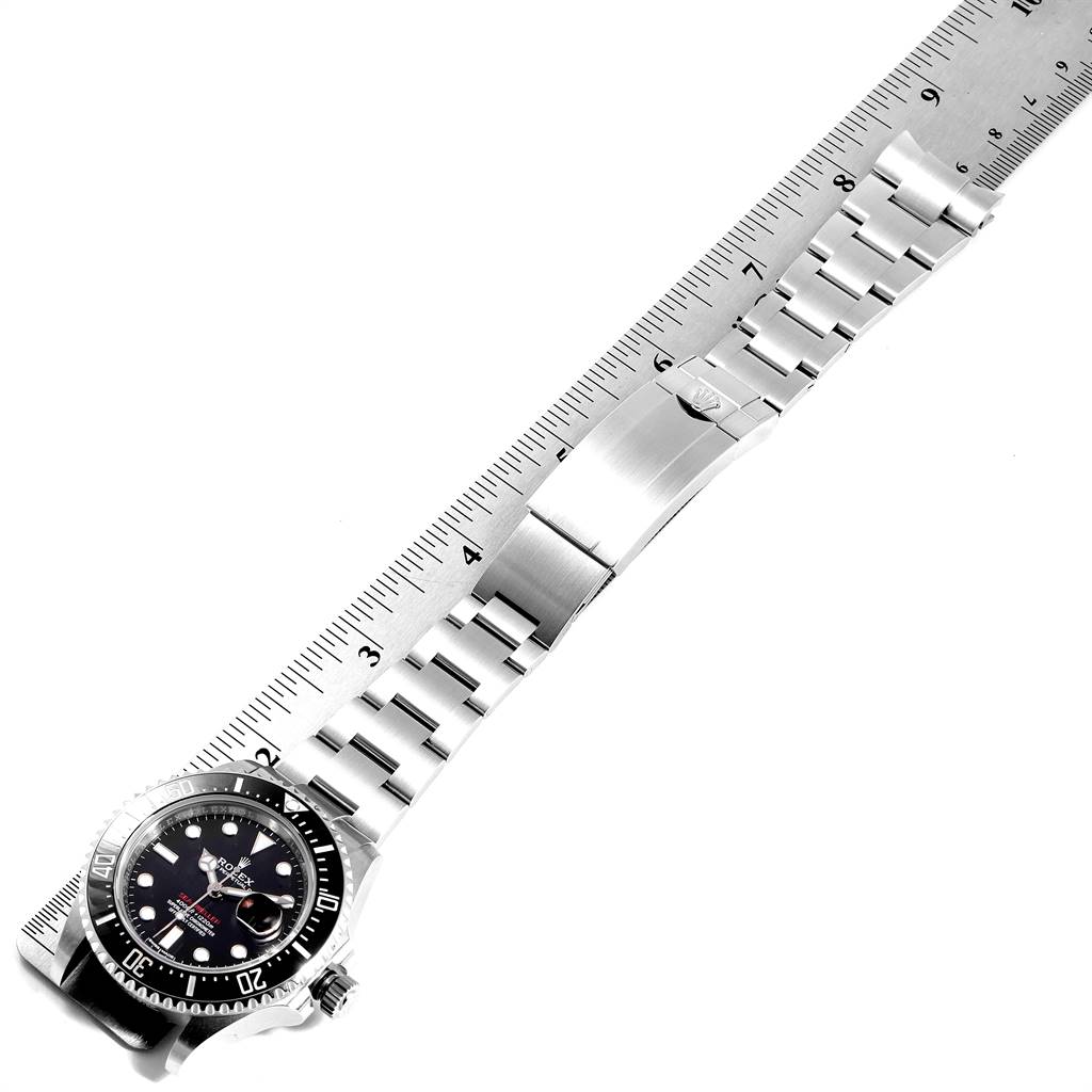 The image shows the Rolex Sea-Dweller 126600 Men
s Stainless Steel Black Dial 126600 Men
s Stainless Steel Black Dial watch laid flat, displaying its face, bezel, and metal bracelet extended along a ruler for measurement.