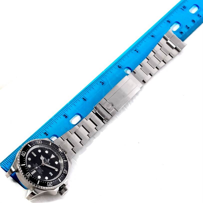 The Rolex Sea-Dweller 116660 Men's Stainless Steel Black Dial 116660 Men's Stainless Steel Black Dial watch is shown from a top-down angle, with its dial and metal bracelet extended alongside a blue ruler.