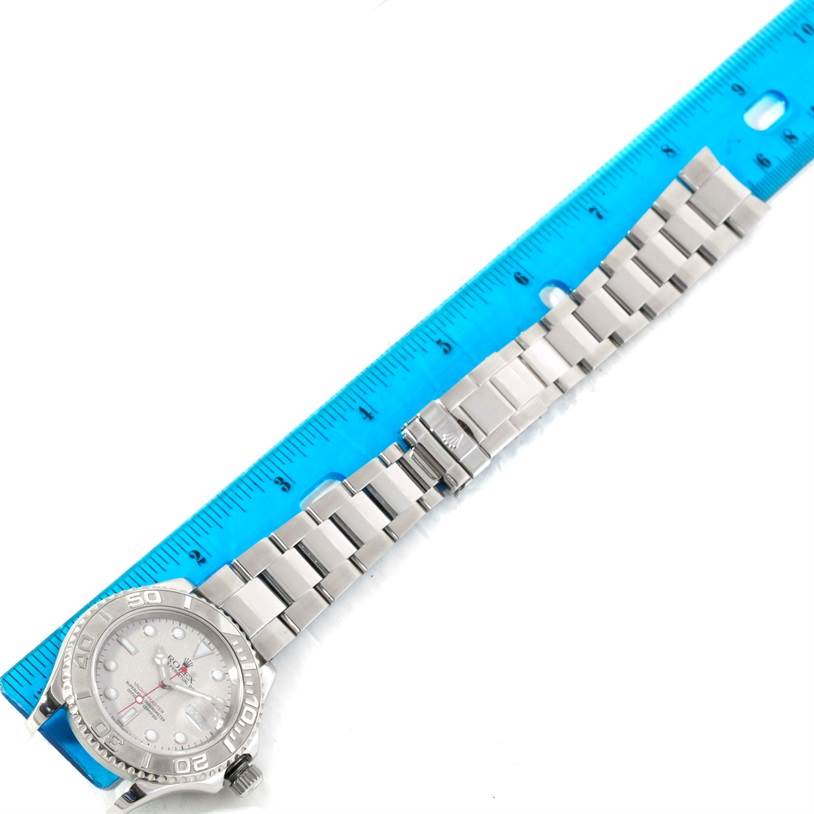 The Yacht-Master Rolex watch is shown lying flat with the dial, bracelet, and clasp visible next to a blue measuring ruler.