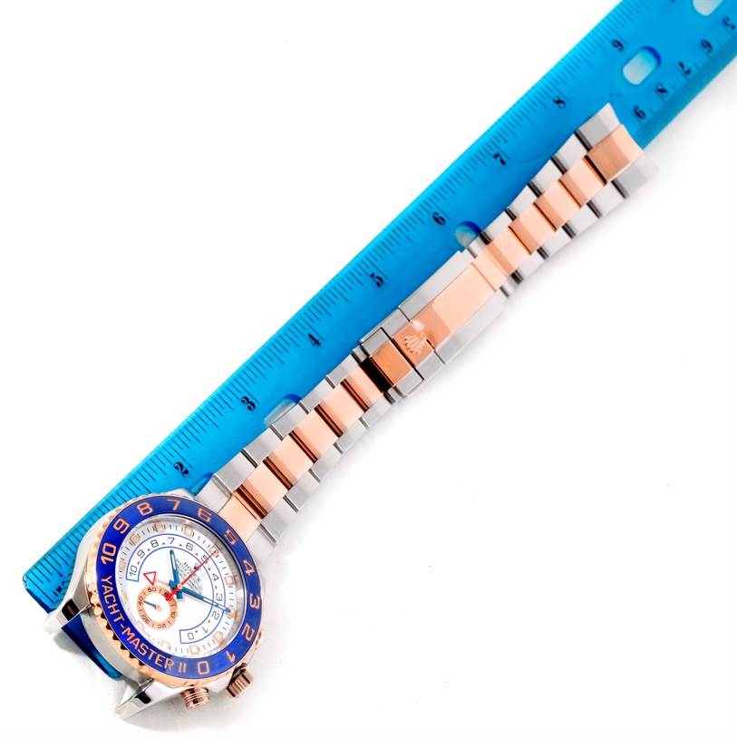 The image shows a top view of a Rolex Yacht-Master 116681 Men's Steel and Gold (two tone) White Dial 116681 Men's Steel and Gold (two tone) White Dial watch with a two-tone band, next to a blue ruler.