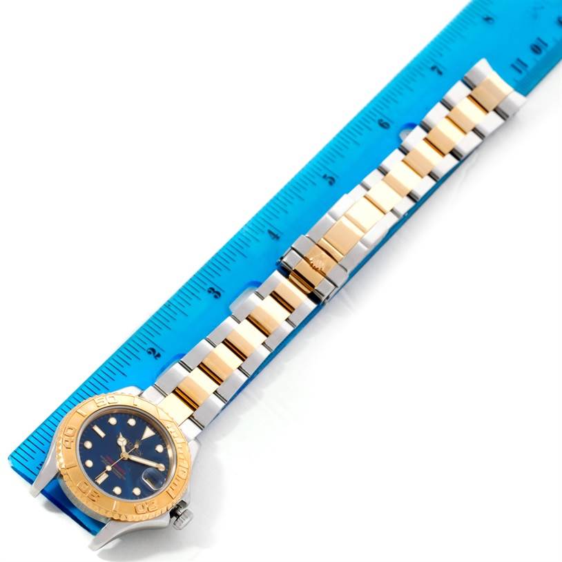 The Rolex Yacht-Master 68623 Men's Stainless Steel Blue Dial 68623 Men's Stainless Steel Blue Dial watch is shown from a top view, highlighting its dial, bezel, and metal bracelet alongside a blue ruler.