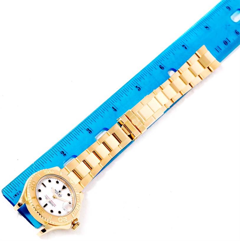 This image shows a Rolex Yacht-Master 68628 Men's Yellow Gold White Dial 68628 Men's Yellow Gold White Dial watch laid flat against a ruler, displaying its gold bracelet and case.