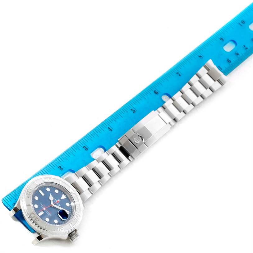 The Rolex Yacht-Master 116622 Men's Stainless Steel Blue Dial 116622 Men's Stainless Steel Blue Dial watch is shown from an overhead angle, highlighting its metal bracelet and clasp next to a blue ruler.