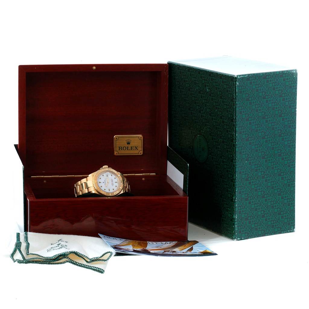 The Yacht-Master Rolex watch is shown inside an open wooden box, alongside a green outer box and accompanying accessories.