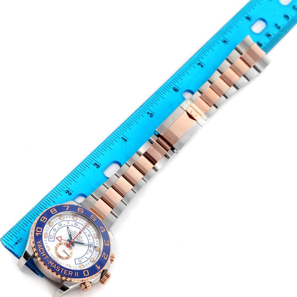 The image shows a top-down view of a Rolex Yacht-Master 116681 Men
s Steel and Gold (two tone) White Dial 116681 Men
s Steel and Gold (two tone) White Dial watch alongside a blue ruler.